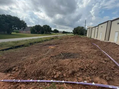Purple drip line laid across freshly graded soil beside a commercial building
