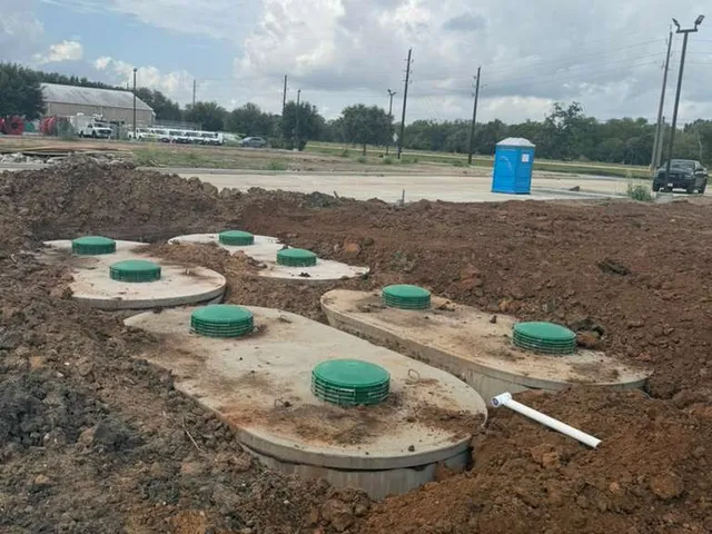 Multiple septic tanks with green lids installed on a graded commercial site