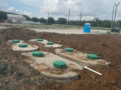 Multiple septic tanks with green lids installed on a graded commercial site