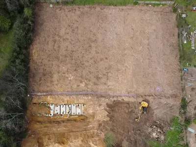 Aerial view of a drain field site with a trench and excavator at work