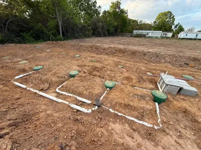 White PVC piping and green risers across a cleared septic field