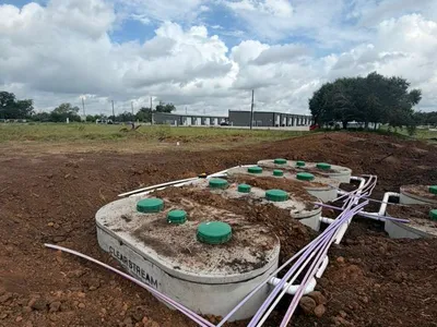 Concrete septic tank with green risers and purple lines in freshly graded soil