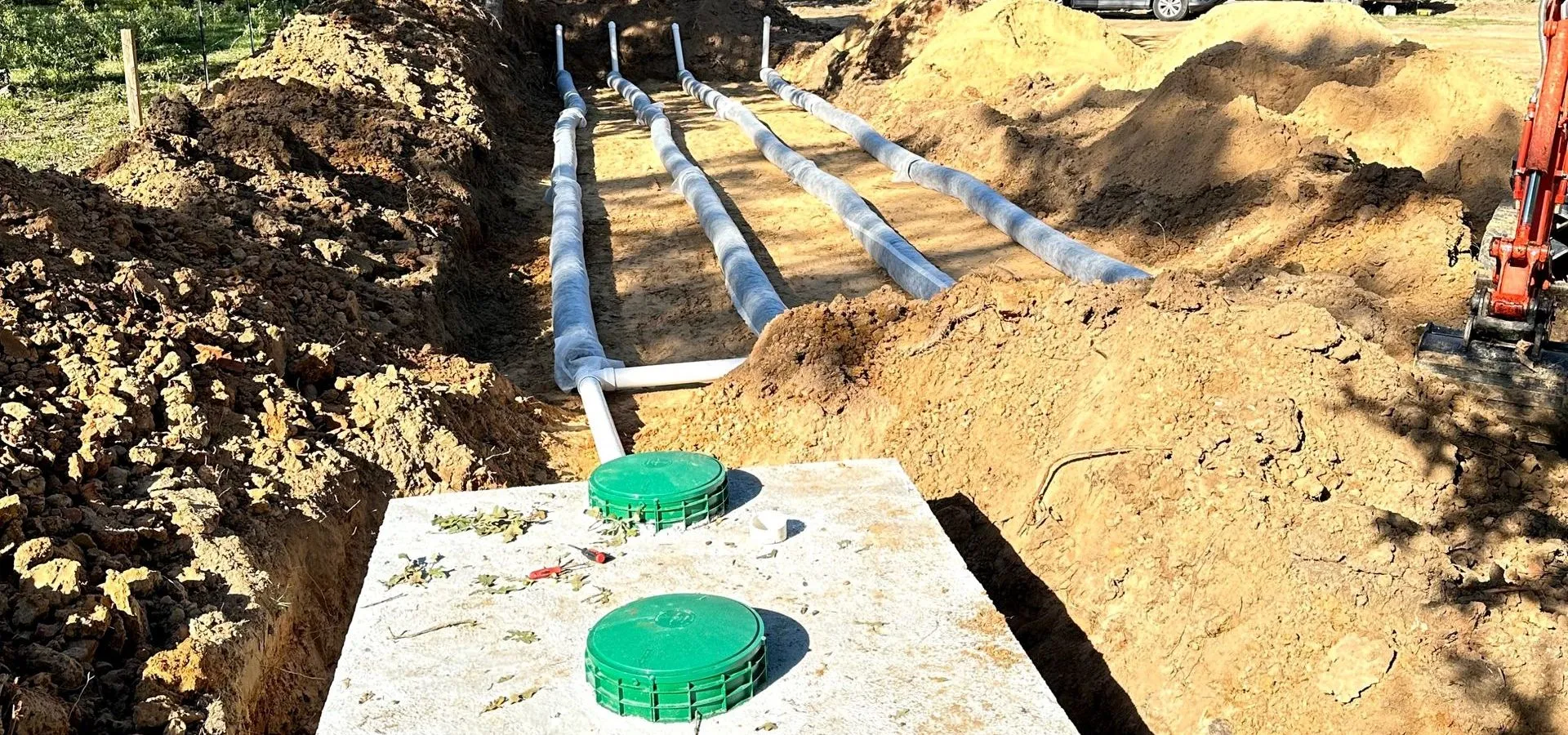 Septic tank with green lids and drainfield lines in an open trench, installed by Engineered Septics in Texas