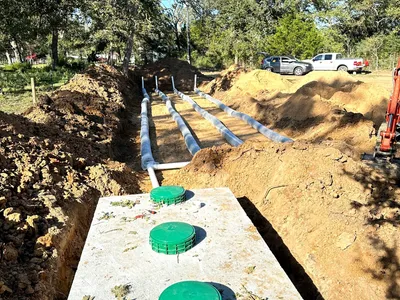 Septic tank with green risers and drainfield lines in an open trench