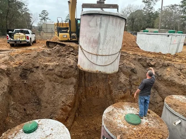 Excavator lowering a concrete septic tank into the ground during installation